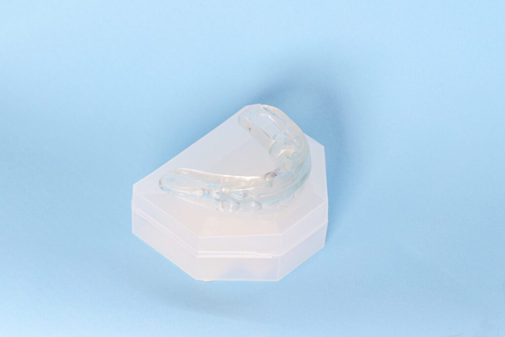 A clear mouthguard on top of a white case in a blue background.